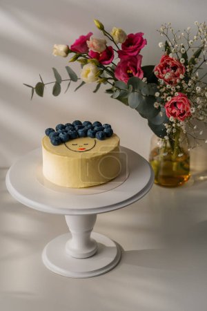 Foto de Delicioso pastel de galletas recién preparado bento decorado con bayas se encuentra en un soporte sobre fondo blanco con flores - Imagen libre de derechos