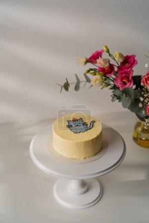 Téléchargez les photos : Délicieux gâteau de biscuit bento fraîchement fait avec un chat peint debout sur un stand sur fond blanc avec des fleurs - en image libre de droit