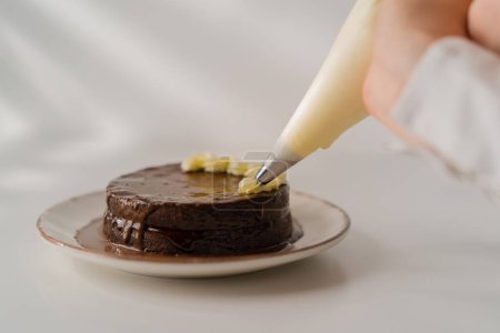 Téléchargez les photos : Délicieux gâteau au chocolat fraîchement fait Sacher ou Prague sur un fond blanc décoré avec de la crème à partir de manches de pâtisserie - en image libre de droit
