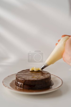 Photo for Delicious freshly made chocolate Sacher or Prague cake on a white background decorated with cream from pastry sleeve - Royalty Free Image