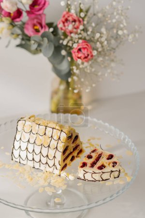 Foto de Delicioso pastel de cereza decorado con virutas de almendras en un soporte cortado pieza sobre fondo blanco con flores - Imagen libre de derechos