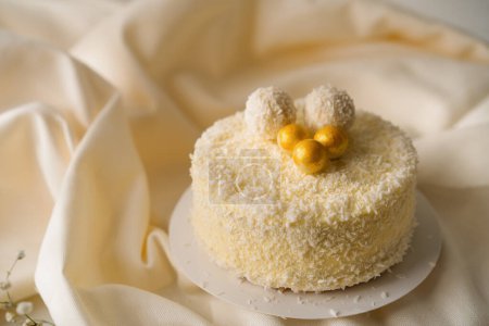 Foto de Delicioso pastel de esponja crema fresca decorada con caramelos de coco fondo de tela beige primer plano - Imagen libre de derechos