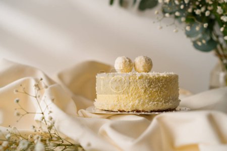Téléchargez les photos : Délicieux gâteau éponge à la crème fraîchement fait décoré avec des bonbons de copeaux de noix de coco sur fond de fleurs - en image libre de droit