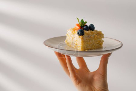 Foto de Rebanada de pastel recién hecho hojaldre delicioso Napoleón pastel con fresas y bayas en el plato en la mano - Imagen libre de derechos