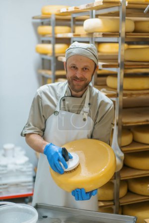 Téléchargez les photos : Fromager souriant en gants nettoie le fromage avec une brosse dans l'entrepôt de la ferme laitière Production laitière Entreprise agricole prospère - en image libre de droit