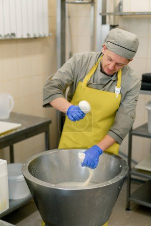 Téléchargez les photos : La production de fromages laitiers le fromager enlève la mozzarella blanche d'une cuve métallique avec ses mains serre gonfle une boule - en image libre de droit