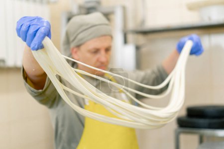 Téléchargez les photos : Production de fromages laitiers le fromager sculpte la mozzarella fraîche avec ses mains et étire le fromage - en image libre de droit