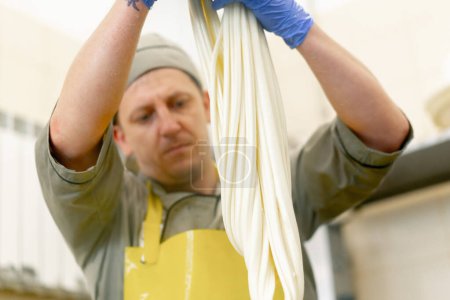 Téléchargez les photos : Production de fromages laitiers le fromager sculpte la mozzarella fraîche avec ses mains et étire le fromage - en image libre de droit