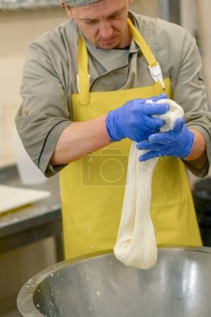 Foto de Producción de quesos lácteos el quesero esculpe mozzarella fresca con las manos y estira el queso - Imagen libre de derechos