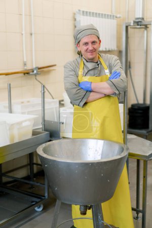 Téléchargez les photos : Un fromager souriant dans un uniforme à la production de fromages laitiers se tient près de l'équipement avant de commencer les travaux - en image libre de droit
