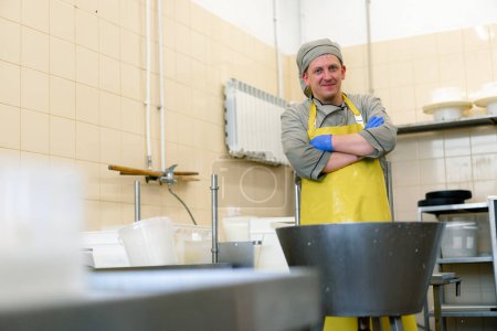 Foto de Una quesera sonriente en uniforme en la producción de quesos lácteos se encuentra cerca del equipo antes de comenzar el trabajo - Imagen libre de derechos