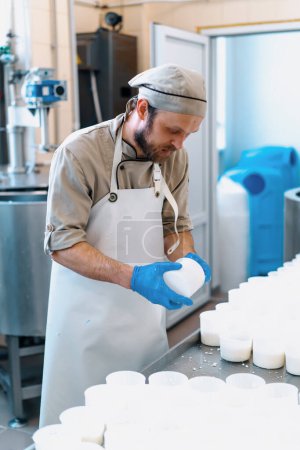 Foto de Un trabajador de una fábrica de quesos artesanales entrega queso en blanco producción de queso blando - Imagen libre de derechos