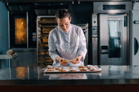 Téléchargez les photos : Belle femme boulanger larmes prêt fraîchement cuit chaud pains aromatiques vérifie la production de pâte boulangerie - en image libre de droit