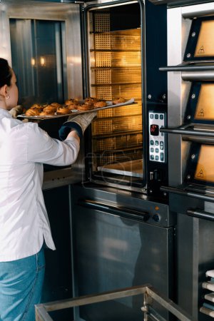 Foto de Panadero atractivo toma panecillos listos y croissants producción de panadería horno profesional productos horneados frescos - Imagen libre de derechos