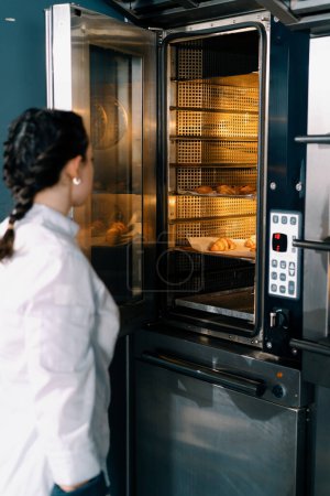 Téléchargez les photos : Attrayant boulanger prend brioches prêtes et croissants professionnel four boulangerie production produits de boulangerie frais - en image libre de droit