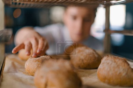 Foto de Atractiva hembra panadero entre estantes buscando y comprobando pan recién horneado muy cuidadosamente industria panadería - Imagen libre de derechos