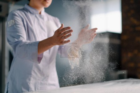 Foto de Un chef experimentado se aplica harina en las manos antes de hacer pan en una panadería prepara pasteles en la cocina profesional - Imagen libre de derechos