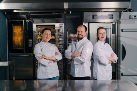 Photo for A team of smiling professional bakers in a professional kitchen in a bakery before the start baking production - Royalty Free Image