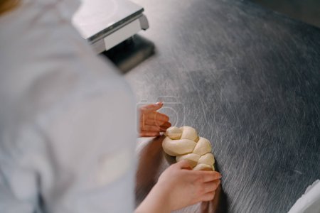 Foto de Panadero forma una trenza de masa cruda en la cocina pasteles de producción de panadería de cocina profesional - Imagen libre de derechos