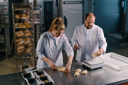 Foto de Dos panaderos dan forma a la masa cruda antes de hornear, cortarlo y rodarlo en la producción de pastelería de cocina profesional de mesa - Imagen libre de derechos