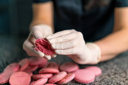 Photo for Female hands breaking almond cookies with hands breaking pink macaron cake with filling in professional kitchen - Royalty Free Image