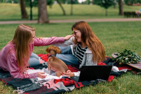 Foto de Dos lesbianas novias descansando en el parque con un pequeño lindo perro y portátil familia picnic gratis amor mascotas al aire libre - Imagen libre de derechos