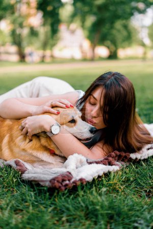 Photo for Young beautiful girl resting in nature lying on a sheet in the park stroking and kissing small corgi dog animals in nature - Royalty Free Image