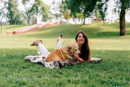 Téléchargez les photos : Jeune belle fille reposant dans la nature couché sur un drap dans le parc jouer avec les petits animaux de chien corgi dans la nature - en image libre de droit