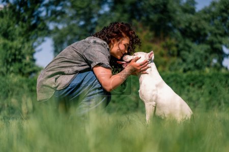 Photo for Beautiful curly girl kisses the nose of a white dog of a large pit bull breed love animals - Royalty Free Image