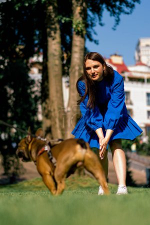 Foto de Una hermosa chica en un paseo con un perro bulldog francés en el parque está jugando con lindo perrito - Imagen libre de derechos