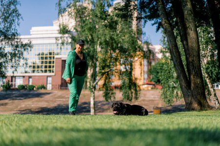 Téléchargez les photos : Un chien obéissant d'une grande race de corso de canne sur une promenade dans un parc d'entraînement pratique commandes avec entraîneur - en image libre de droit