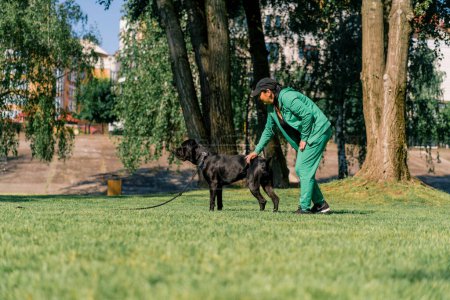 Foto de Un psicólogo perro está junto a un gran perro negro Cane Corso en un paseo por el parque y elogia perro - Imagen libre de derechos
