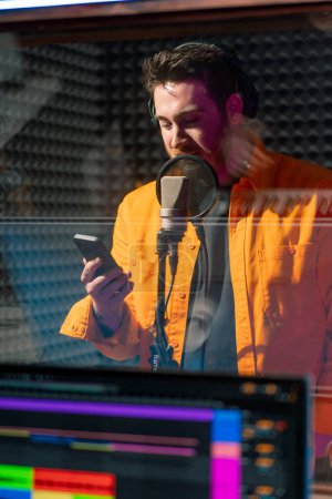 Téléchargez les photos : Jeune rappeur pop enregistrant émotionnellement une nouvelle chanson en studio d'enregistrement professionnel ingénieur du son derrière verre - en image libre de droit