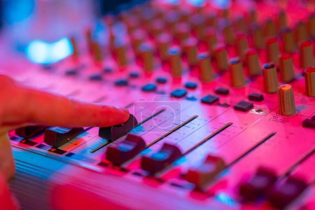 Téléchargez les photos : Studio d'enregistrement professionnel ingénieur du son doigt ajuste le volume sonore mélangeur console égaliseur création musicale néon lumière - en image libre de droit