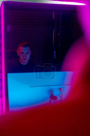 Photo for Recording studio with professional equipment sound engineer sits at the console view through window purple neon light - Royalty Free Image