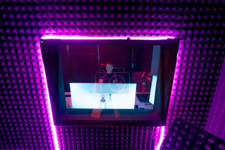 Foto de Estudio de grabación con equipo profesional ingeniero de sonido se sienta en la vista de la consola a través de la luz de neón púrpura ventana - Imagen libre de derechos