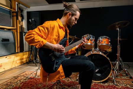 Téléchargez les photos : Portrait de jeune artiste rock avec guitare électrique en studio d'enregistrement jouant sa propre piste instrument de musique batterie arrière-plan - en image libre de droit