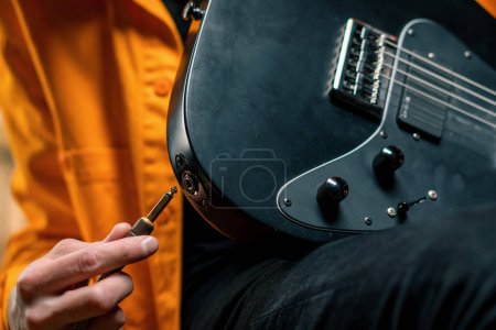 Photo for Rock performer with electric guitar in recording studio holds musical instrument in hands connects with string wire - Royalty Free Image