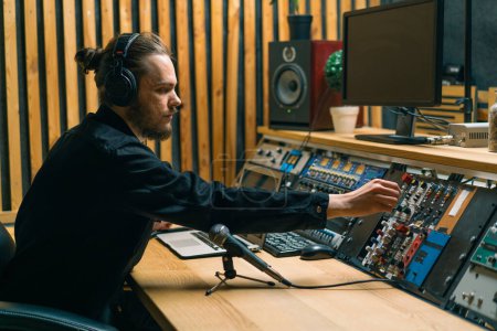 Téléchargez les photos : Jeune ingénieur du son avec écouteurs travaillant dans un studio de musique avec moniteurs et un égaliseur mélangeant des pistes de mastering - en image libre de droit