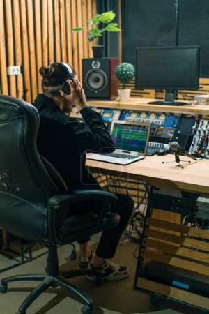 Foto de Joven ingeniero de sonido que se pone auriculares trabajando en un estudio de música profesional con monitores y un ecualizador mezclando pistas de masterización - Imagen libre de derechos