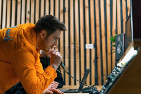 Foto de Joven artista pop rap emocionalmente la grabación de una nueva canción en un estudio de grabación profesional ingeniero de sonido viendo pistas en exhibición - Imagen libre de derechos