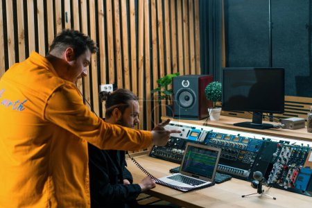Téléchargez les photos : Jeune rappeur pop enregistrant émotionnellement une nouvelle chanson dans un studio d'enregistrement professionnel ingénieur du son regarder des pistes exposées - en image libre de droit