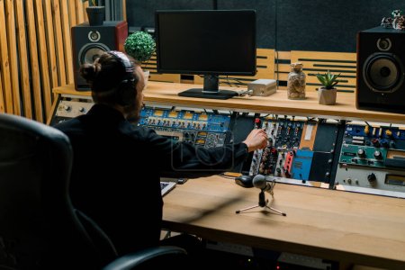 Téléchargez les photos : Jeune ingénieur du son avec écouteurs travaillant dans un studio de musique avec moniteurs et un égaliseur mélangeant des pistes de mastering - en image libre de droit