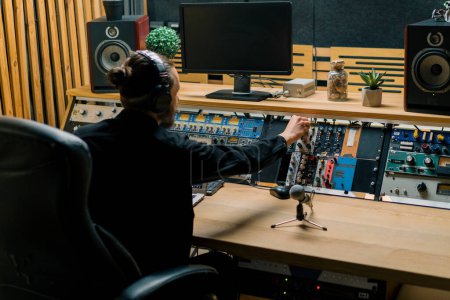 Foto de Joven ingeniero de sonido con auriculares trabajando en un estudio de música con monitores y un ecualizador mezclando pistas de masterización - Imagen libre de derechos