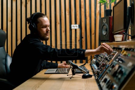 Foto de Joven ingeniero de sonido con auriculares trabajando en un estudio de música con monitores y un ecualizador mezclando pistas de masterización - Imagen libre de derechos