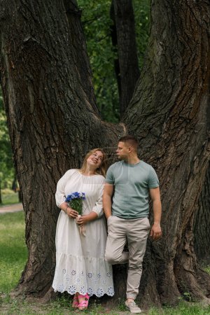 Foto de Retrato de una pareja enamorada de un hombre y una mujer embarazada con flores en el parque, a la espera de una nueva adición a la familia de la pareja se mira entre sí - Imagen libre de derechos