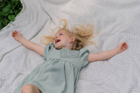 Téléchargez les photos : Portrait d'une fille heureuse couchée sur une couverture dans le parc Visage rêveur d'un enfant un enfant regarde le ciel Sourire vue de dessus de l'enfance - en image libre de droit
