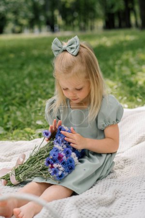 Téléchargez les photos : Portrait d'une petite fille heureuse reposant dans le parc avec des fleurs sans soucis enfance journée d'été loisirs en plein air - en image libre de droit