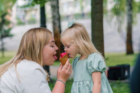 Photo for Little cute girl green summer dress eating delicious ice cream with mom in city park summer family lifestyle Childhood - Royalty Free Image