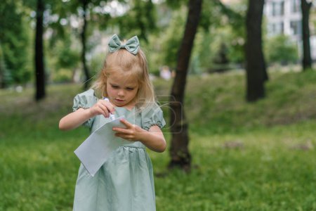 Photo for Portrait of an angry upset capricious girl in a dress in the park draws a postcard with felt-tip pen gets annoyed and sketches everything annoyingly - Royalty Free Image